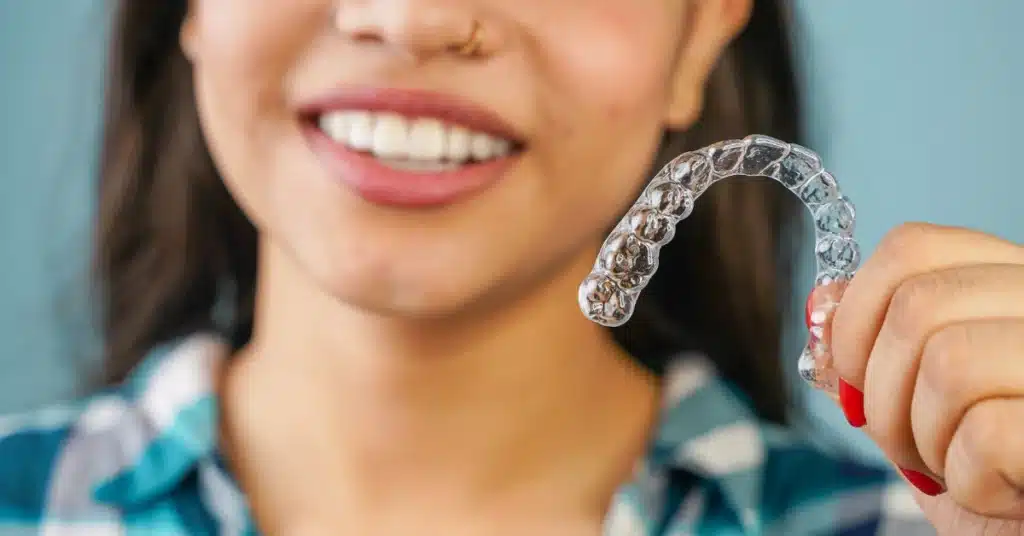 Smiling woman holding a clear Invisalign aligner in her hand, showing how invisible braces are used for discreet teeth straightening.