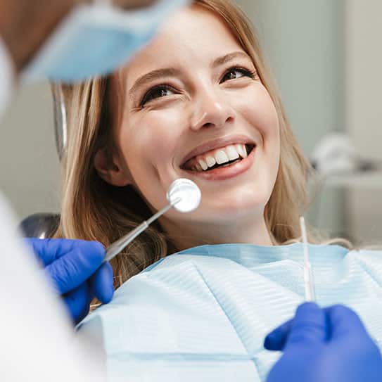 A cheerful patient smiling while a dentist examines her teeth using dental instruments in a modern clinic.