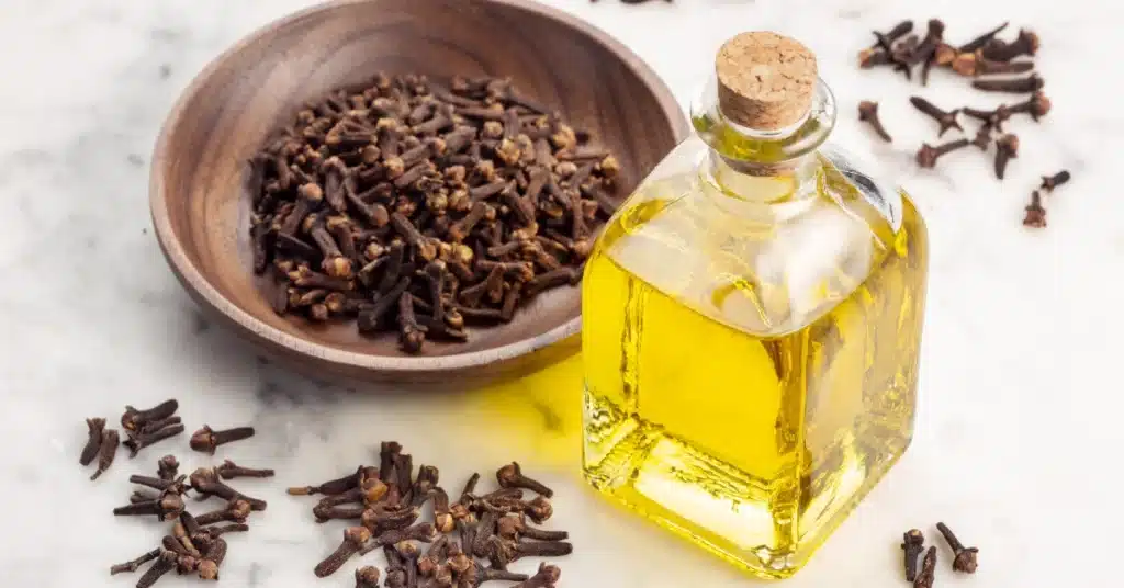 Bottle of clove oil next to dried cloves in a wooden bowl, illustrating a natural remedy for tooth pain relief.