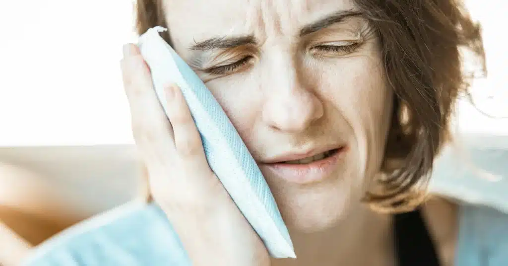 Woman pressing a cold compress against her cheek to relieve swelling and pain caused by a dental issue or toothache.