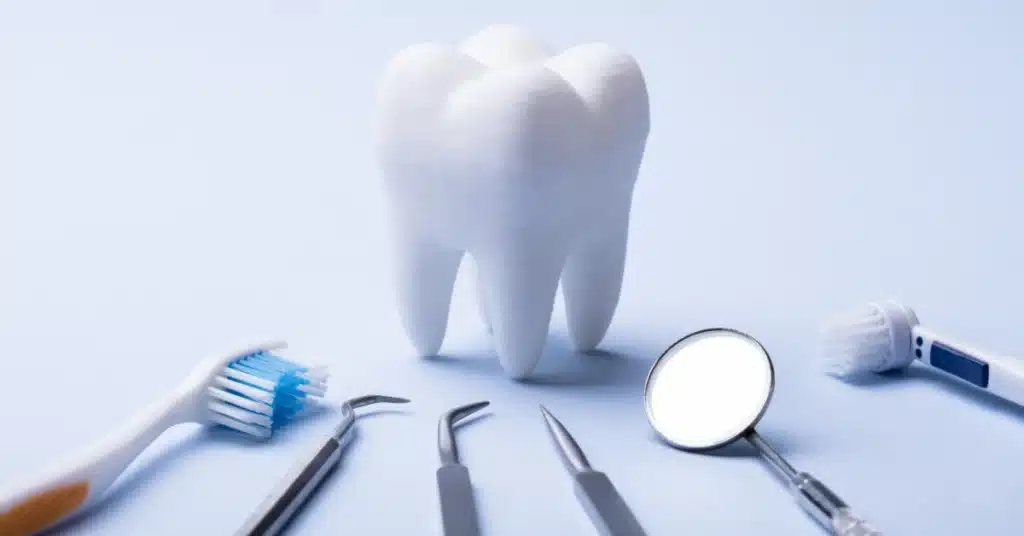 A tooth model with dental tools, including a toothbrush and mirror, on a light blue background.