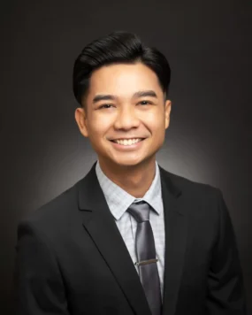 A professional headshot of Dr. Kevin Dionisio, smiling in a suit and tie against a dark background.