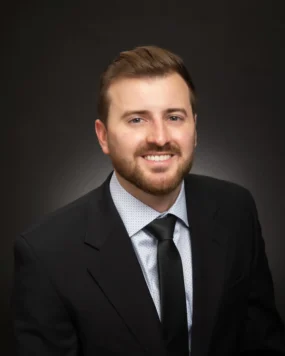 A professional headshot of Dr. Kevin Major, smiling in a suit and tie against a dark background.