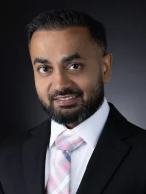 A professional headshot of Dr. Rahul Patel, smiling in a suit and tie against a dark background.