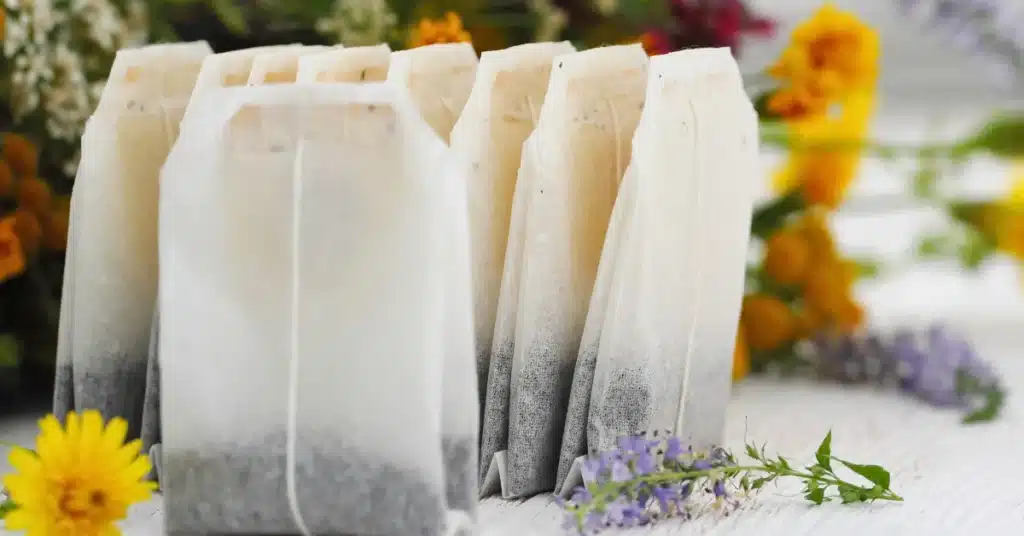 A row of herbal peppermint tea bags arranged on a white wooden surface with colorful flowers in the background.