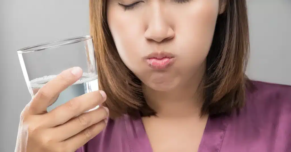 Woman rinsing her mouth with a hydrogen peroxide solution, holding a glass of liquid to demonstrate an oral rinse for disinfecting and soothing gums.