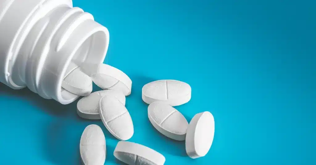 White pain relief tablets spilled from a bottle onto a blue surface, representing over-the-counter medications used for dental pain or discomfort.