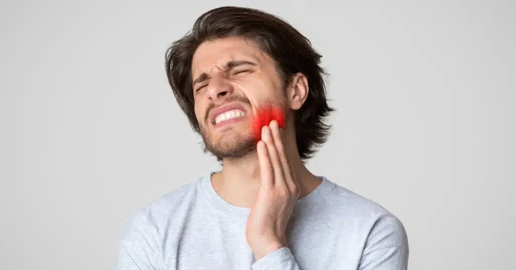 Young man clenching his jaw and holding his cheek in pain, with red highlight showing TMJ discomfort or inflammation