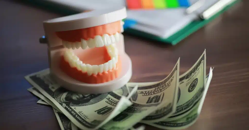 A dental model with white teeth placed on top of several U.S. hundred-dollar bills, symbolizing the cost of dental care or treatment financing options.